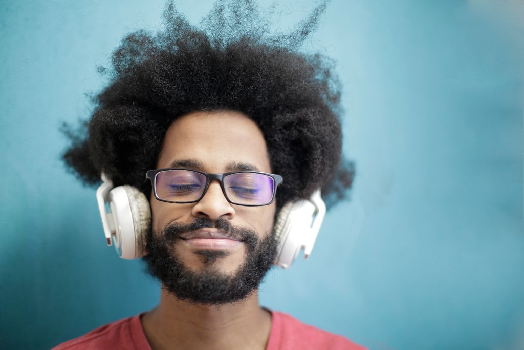 A joyful man with afro hair enjoying music with headphones, eyes closed, and a smile.