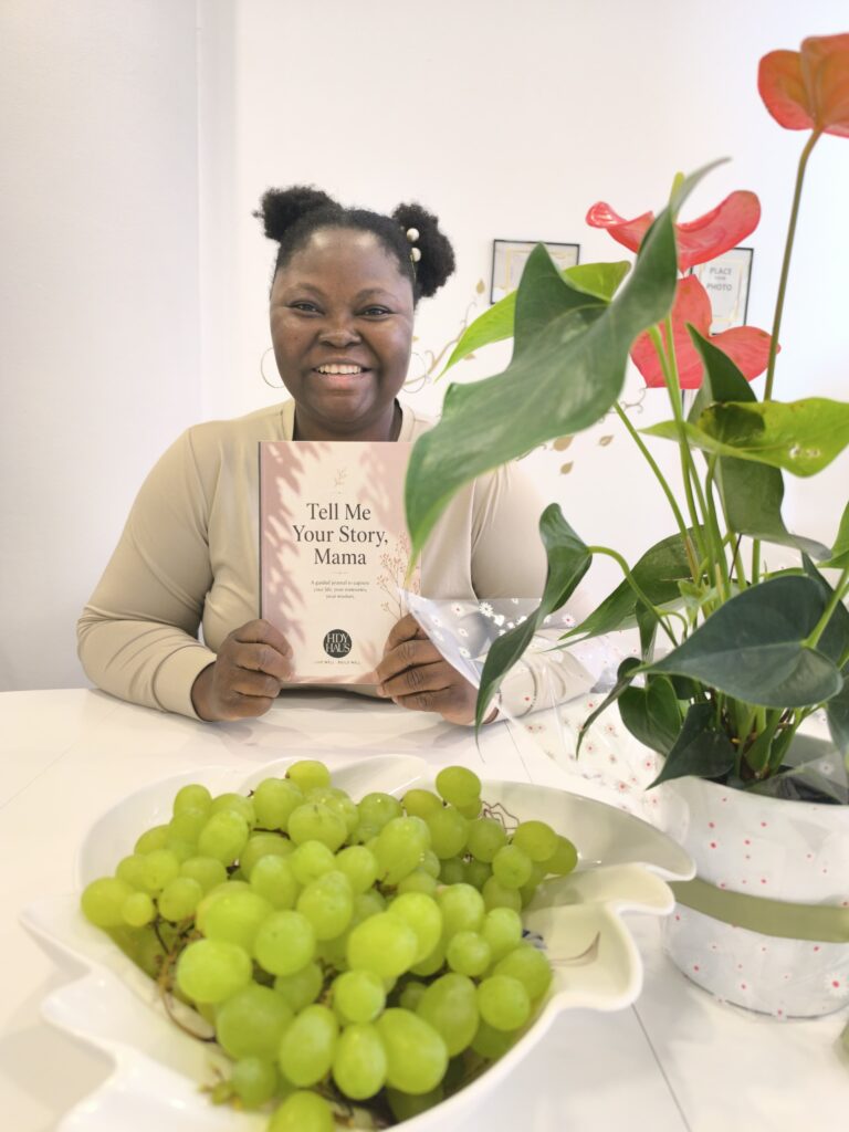 A Photo of myself holding a copy of Tell Me Your Story, Mama which is published by HDY Haus and written by yours truly, Mary Mojisola Job