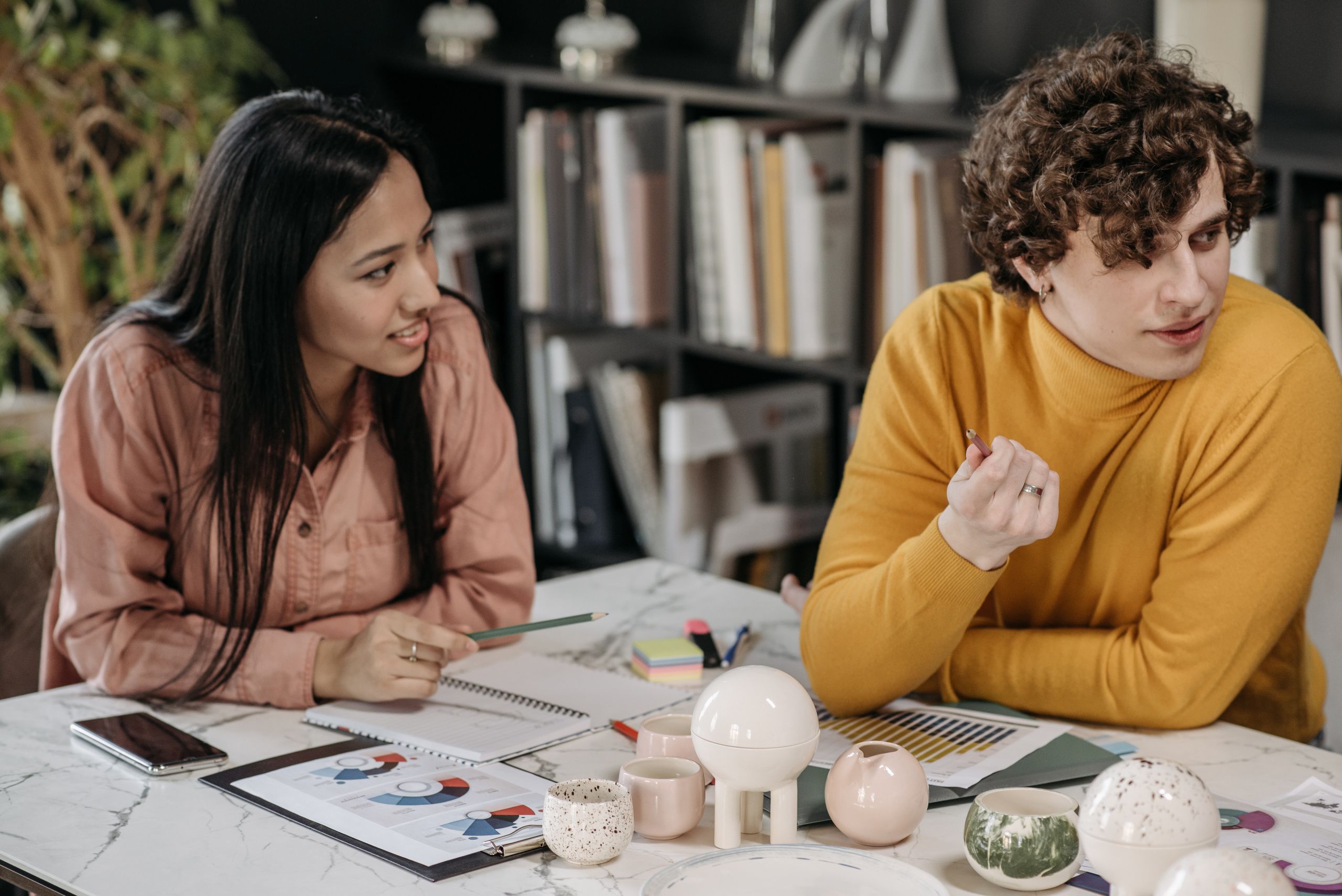 Asian woman and caucasian man in a creative office meeting discussing community management vs community strategising